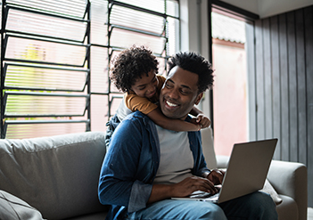 Man with laptop on lap smiling at child on his back.